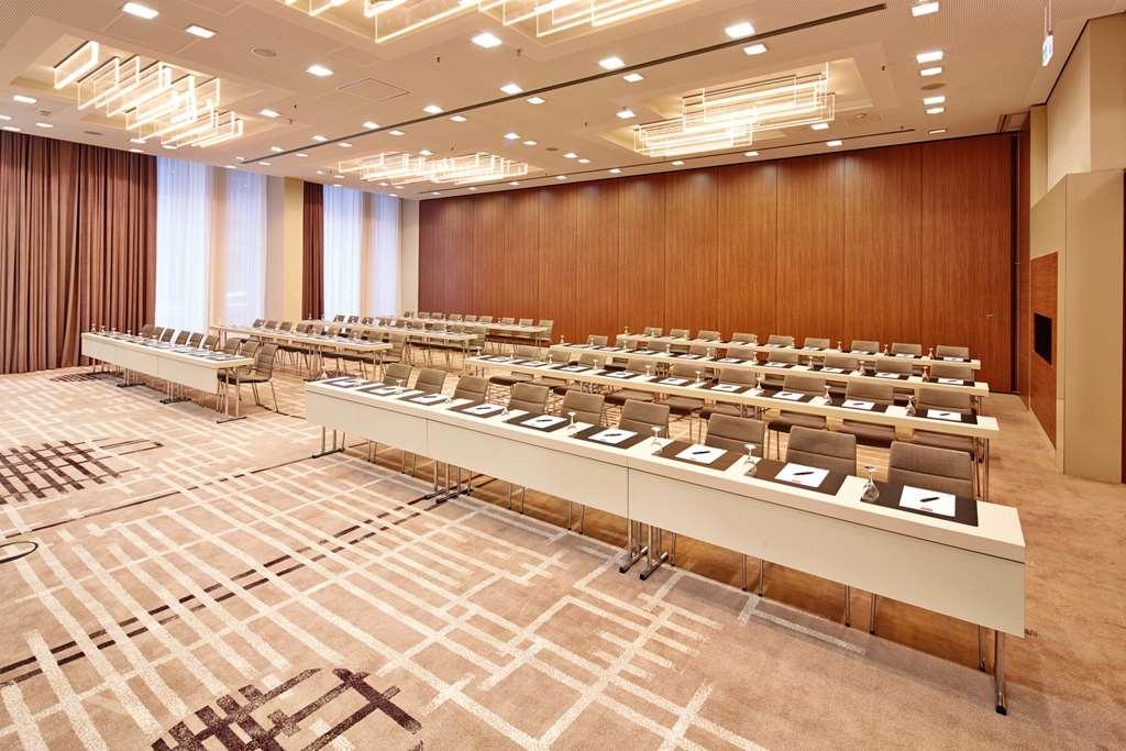 Steigenberger Hotel Am Kanzleramt Berlin Facilities photo The photo shows a modern conference room set up for a meeting or seminar. There are multiple rows of long, white tables arranged in a rectangular layout, each equipped with chairs. On the tables, there are items like notepads and pens, indicating a p