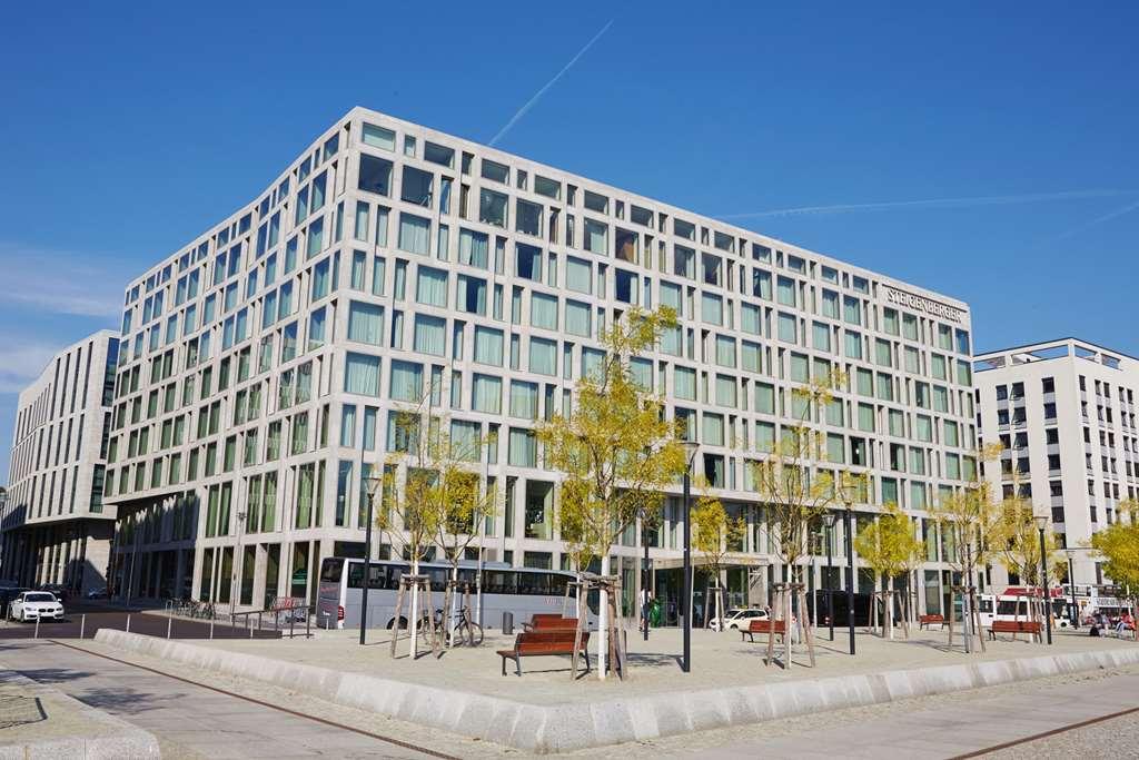 Steigenberger Hotel Am Kanzleramt Berlin Exterior photo The image shows a modern building with a distinctive architectural design. The building has large glass windows arranged in a grid pattern, giving it a sleek and contemporary look. In front of the building, there are several small, leafy trees and be