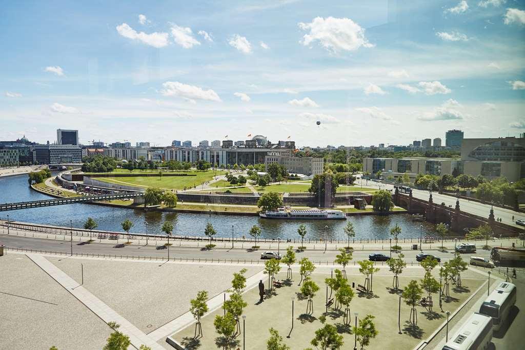 Steigenberger Hotel Am Kanzleramt Berlin Facilities photo The photo shows a vibrant urban landscape featuring a river that curves through the scene. On one side of the river, there is a green park area, likely with trees and open spaces. In the background, modern buildings stretch along the riverbank. The s