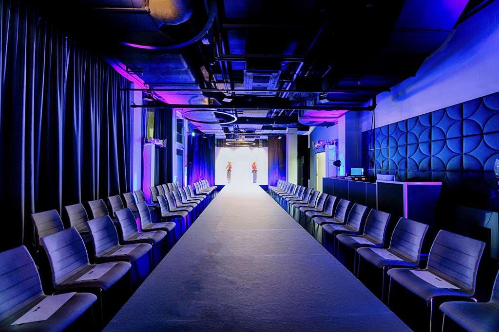 Steigenberger Hotel Am Kanzleramt Berlin Facilities photo The photo shows a fashion runway setup. There's a long, narrow runway stretching down the center, flanked by rows of modern chairs on either side. The space is dimly lit, with dramatic purple and blue lighting creating an atmosphere suited for a fash