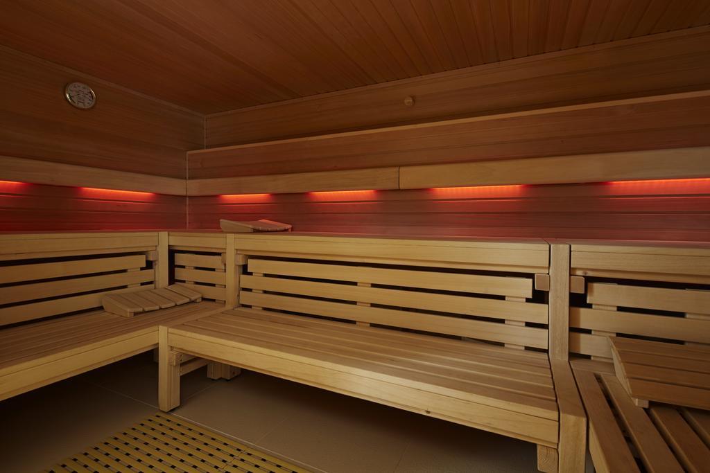 Steigenberger Hotel Am Kanzleramt Berlin Exterior photo The photo shows the interior of a sauna. The walls and benches are made of light-colored wood, creating a warm and natural atmosphere. There are horizontal wooden slats forming the benches, which are arranged for seating. Soft red lighting is install