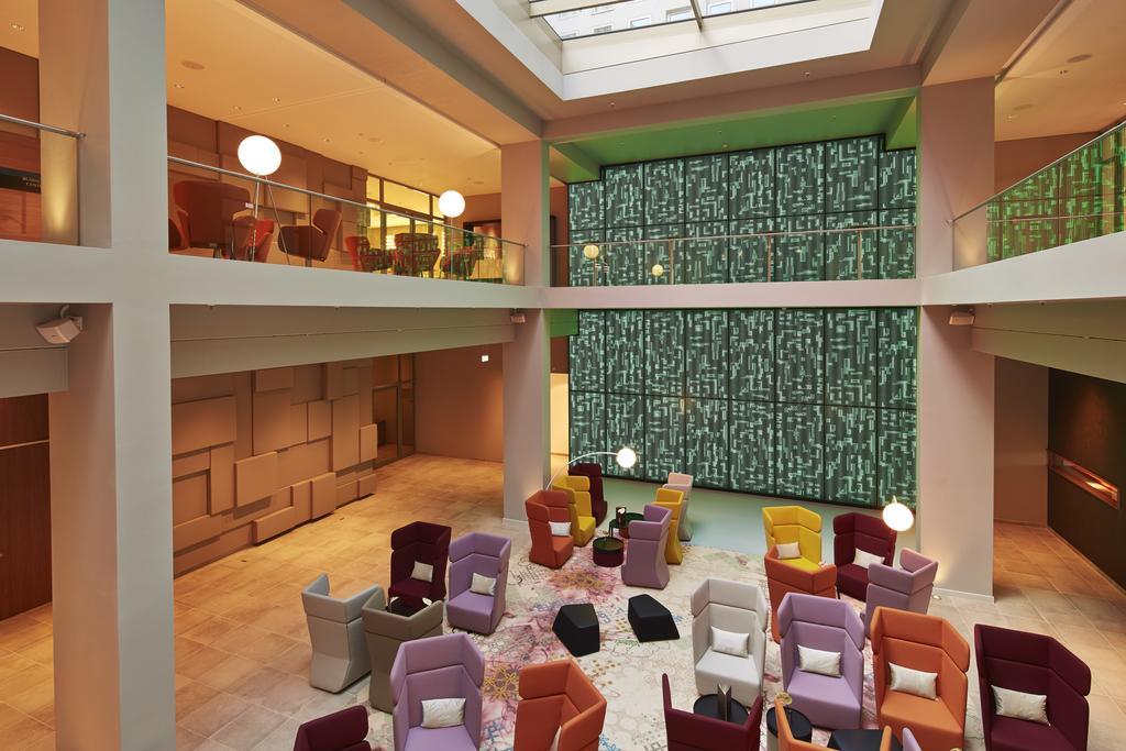 Steigenberger Hotel Am Kanzleramt Berlin Exterior photo The photo depicts a modern, stylish interior space, likely a hotel or lounge area. It features a large open area with multiple seating arrangements consisting of colorful armchairs in various shapes and styles. The color palette includes shades of re